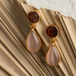 Gold earrings with brown and pink stones on a textured beige surface