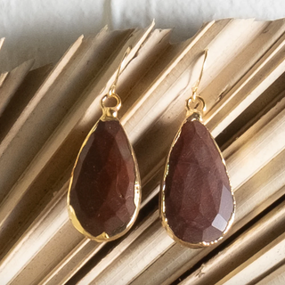 Teardrop-shaped earrings with gold accents on a textured surface