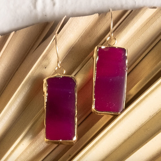 Gold-framed purple earrings on a wooden surface