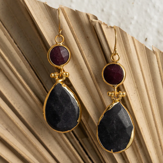 Pair of earrings with gold accents, red gemstones, and black stones on a textured surface.