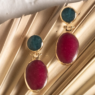 Gold earrings with red and blue stones on a gold surface