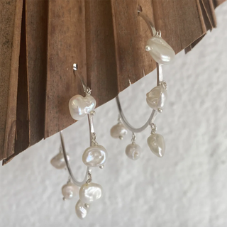 Pearl earrings hanging on a wooden surface with a white fabric background
