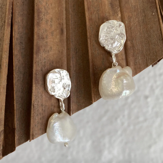 Pearl earrings with textured silver tops on a wooden surface