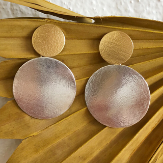 Gold and silver round earrings on a textured surface